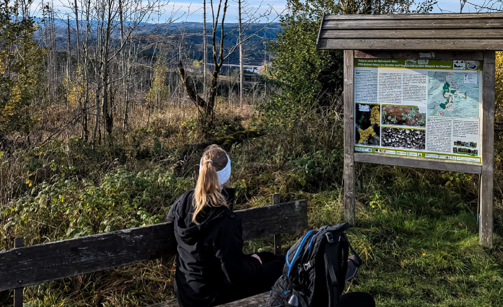 Frau sitzt mit dem Rücken zum Betrachter auf einer Bank in der Natur und schaut auf eine Talsperre.